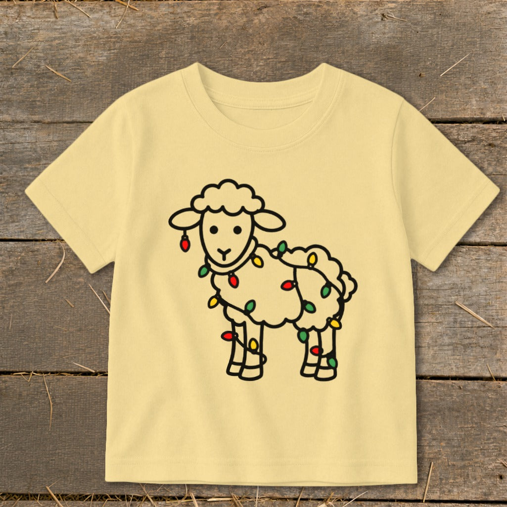 A light yellow children's t-shirt features a line drawing of a sheep tangled in Christmas lights.