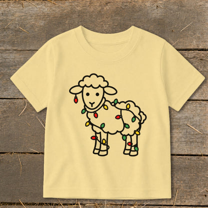 A light yellow children's t-shirt features a line drawing of a sheep tangled in Christmas lights.