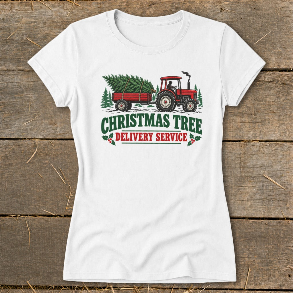White t-shirt graphic with red tractor pulling Christmas tree, text "Christmas Tree Delivery Service".