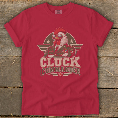 A red short-sleeved t-shirt featuring a graphic of a chicken in a military uniform wearing sunglasses with the text CLUCK COMMANDER.