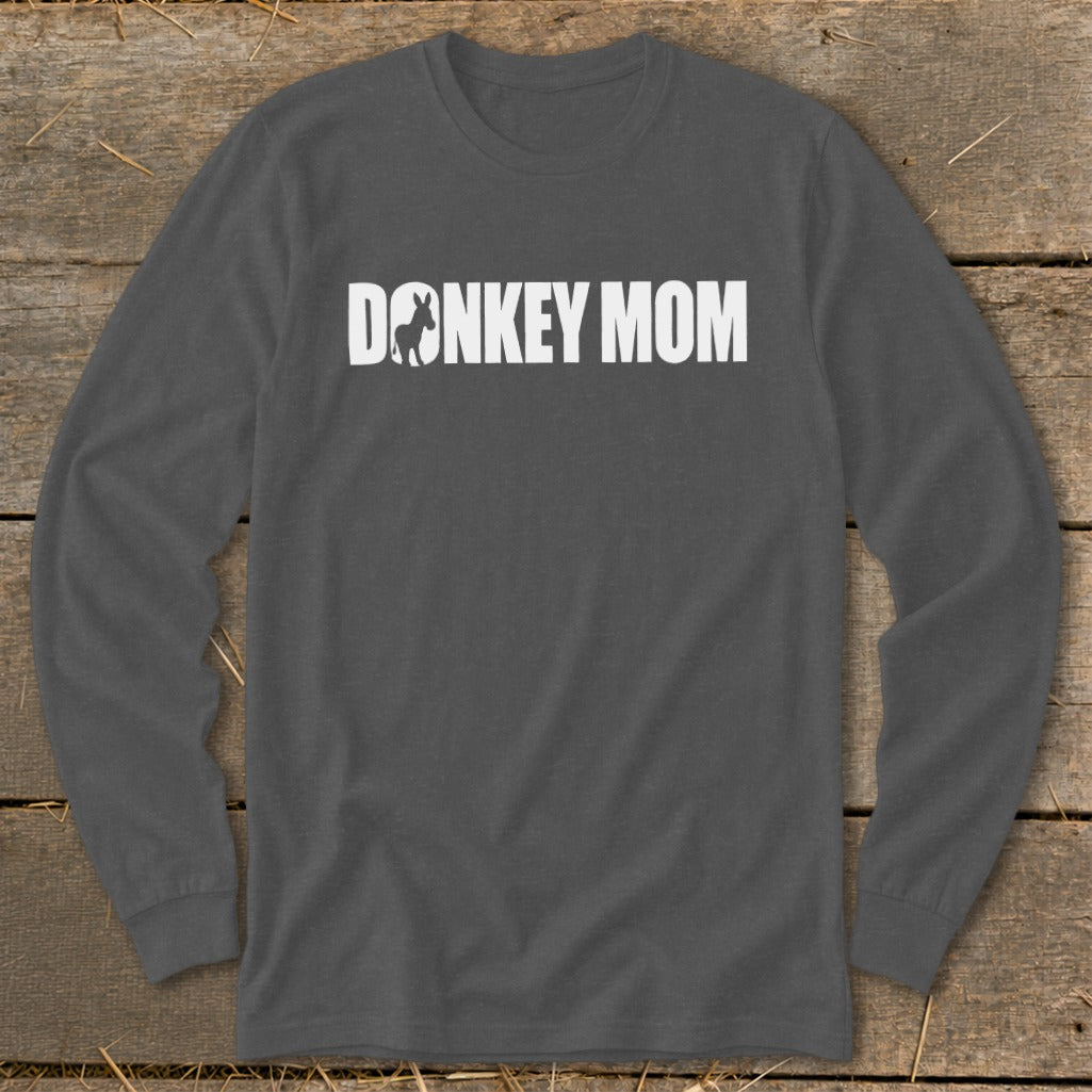 Dark grey long-sleeve t-shirt with white text reading "DONKEY MOM" and a donkey silhouette inside the letter O, laid flat on a rustic wooden surface.