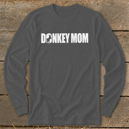 Dark grey long-sleeve t-shirt with white text reading "DONKEY MOM" and a donkey silhouette inside the letter O, laid flat on a rustic wooden surface.