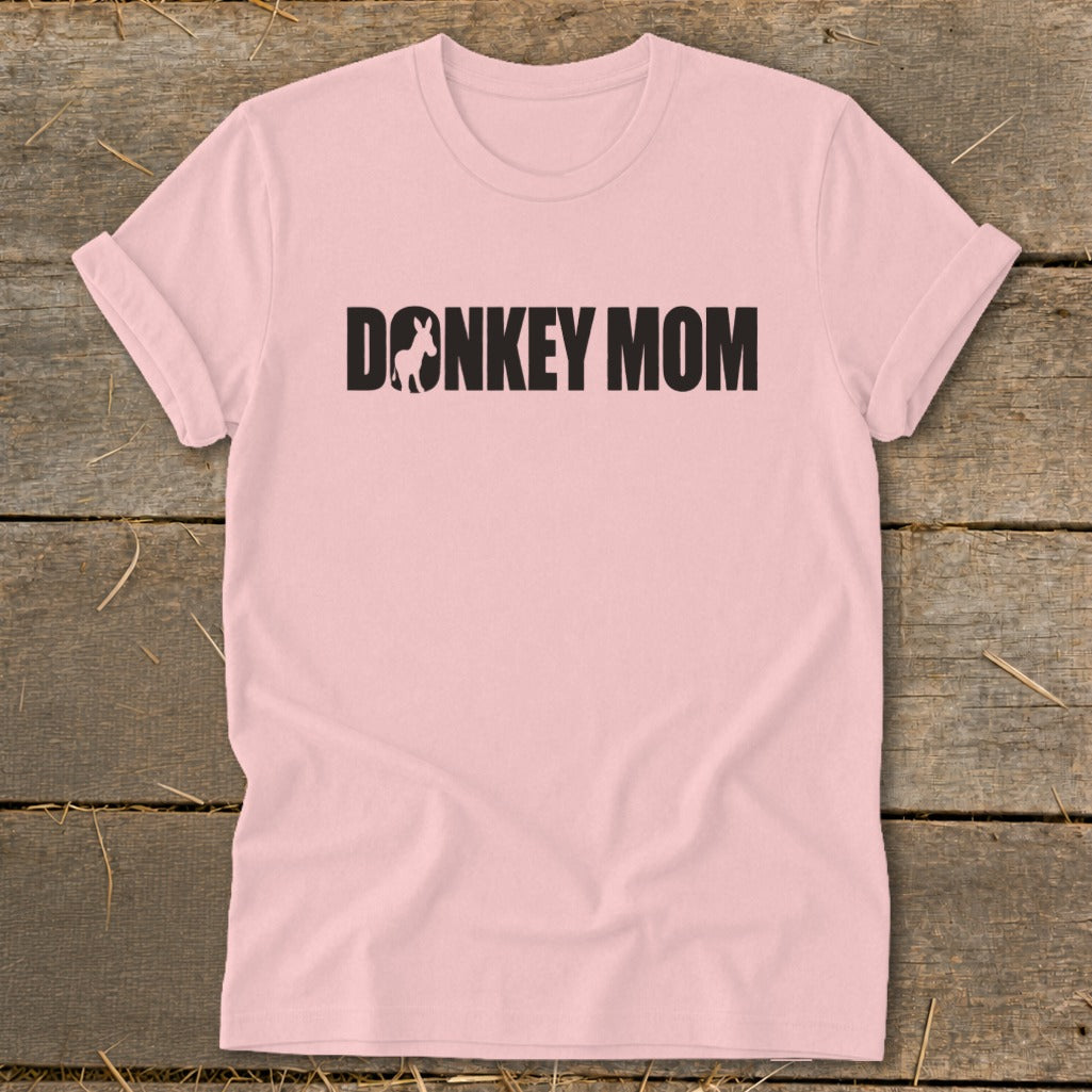 A light pink t-shirt with rolled-up sleeves displays the black text Donkey Mom, featuring a donkey silhouette inside the letter O.