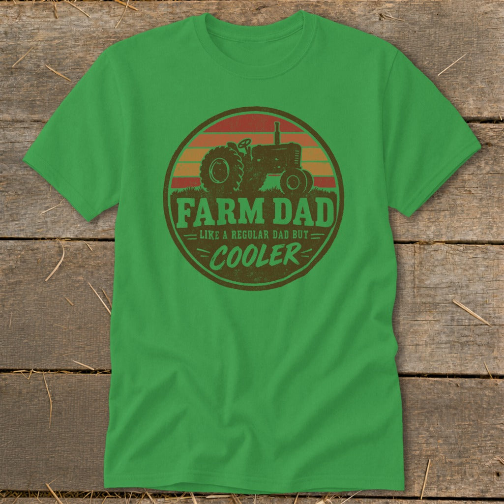 A green t-shirt with a round graphic of a tractor, sunset, and text reading FARM DAD LIKE A REGULAR DAD BUT COOLER.