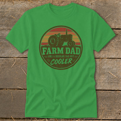 A green t-shirt with a round graphic of a tractor, sunset, and text reading FARM DAD LIKE A REGULAR DAD BUT COOLER.