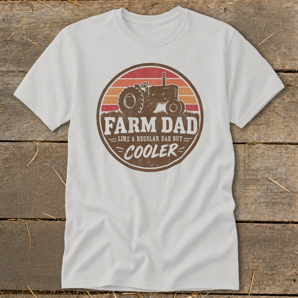 A white t-shirt featuring a retro tractor design with the text FARM DAD LIKE A REGULAR DAD BUT COOLER.