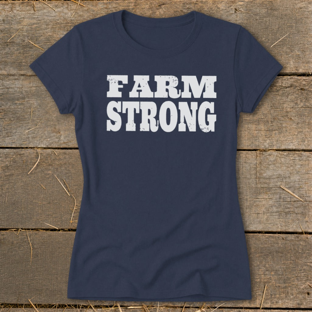 Dark blue women's t-shirt featuring the white distressed text FARM STRONG centered on the chest, laid flat on wooden planks.