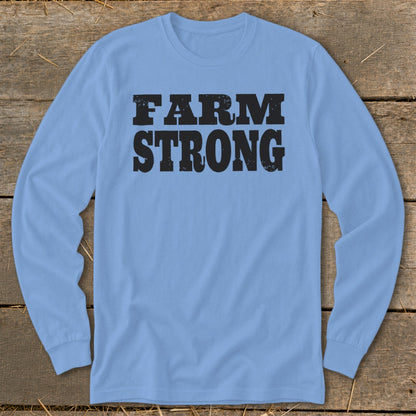 Light blue long-sleeve t-shirt with black distressed text reading FARM STRONG, laid flat on wooden planks.