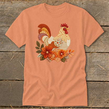 Peach-colored t-shirt featuring a colorful embroidered chicken surrounded by autumn flowers on a wooden background.