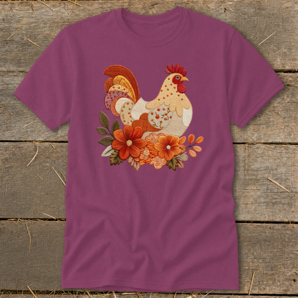 Purple short-sleeved t-shirt featuring a detailed embroidered rooster design nestled among autumn-colored flowers on a rustic wooden background.