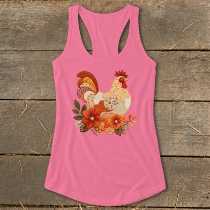 A pink racerback tank top with a decorative embroidered rooster and orange flower graphic on a wooden background.