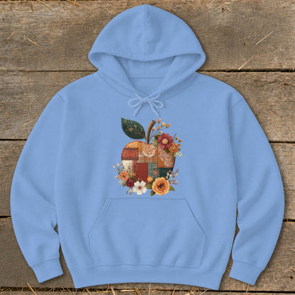 Light blue hoodie with a patchwork apple graphic featuring flowers and leaves.