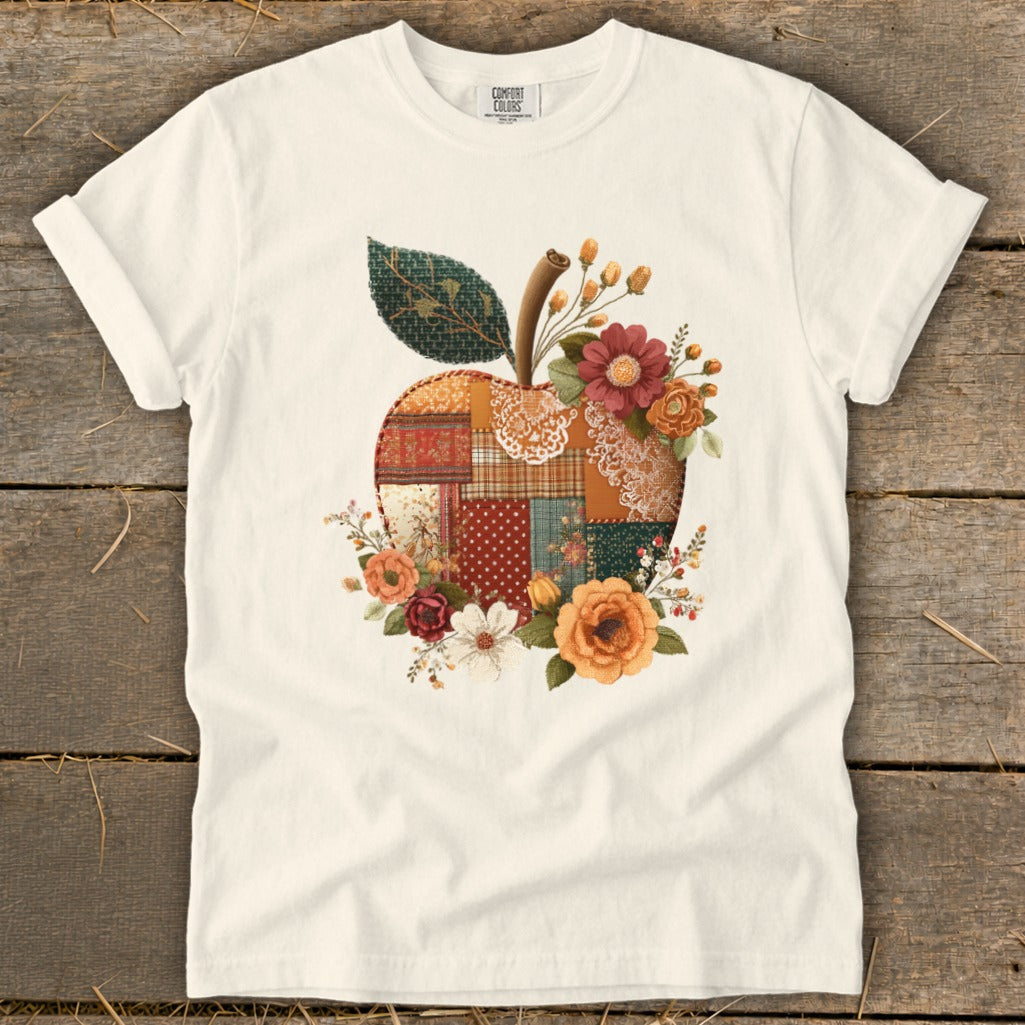 White t-shirt with a patchwork apple graphic and floral accents.