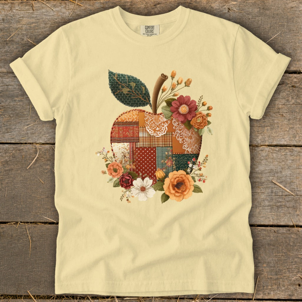 Light yellow t-shirt with a patchwork apple design and floral accents.