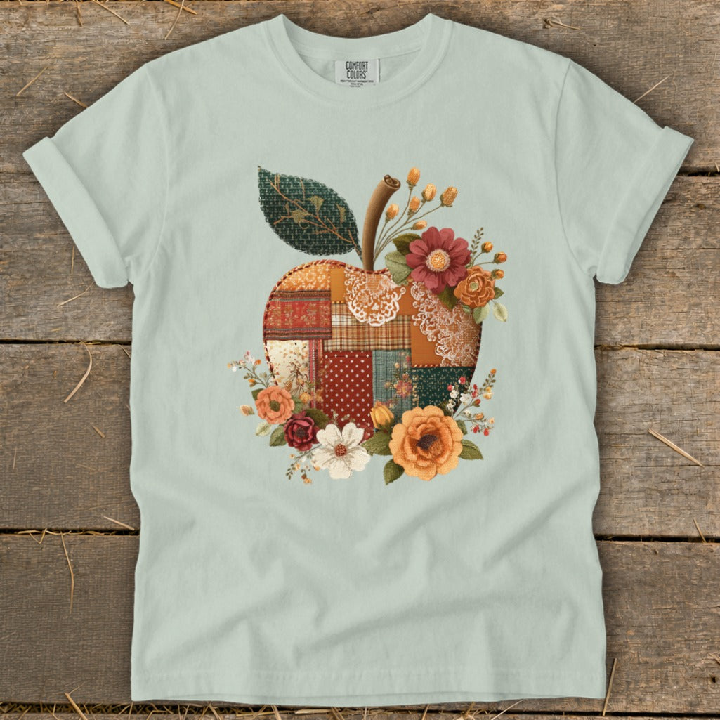 Light green t-shirt featuring a patchwork apple design with flowers and a leaf.