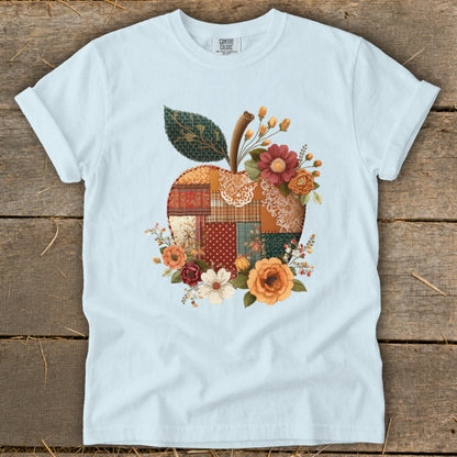 Light blue t-shirt with a patchwork apple graphic adorned with flowers.