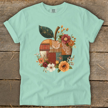 Teal t-shirt with a patchwork apple graphic surrounded by flowers.