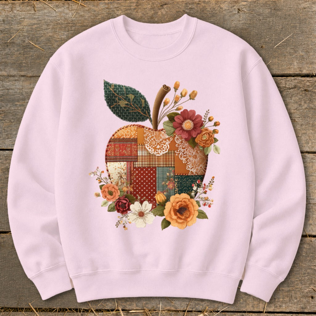 Pink sweatshirt with a patchwork apple design featuring flowers and a leaf.