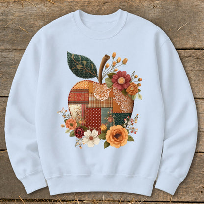 Light blue crewneck sweatshirt featuring a patchwork apple design with floral accents.