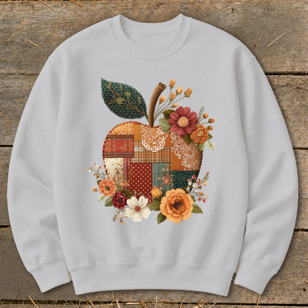 Light gray sweatshirt with a patchwork apple design surrounded by flowers and a leaf.