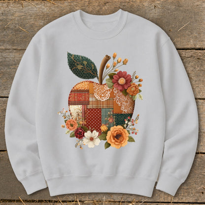Light gray sweatshirt with a patchwork apple design surrounded by flowers and a leaf.