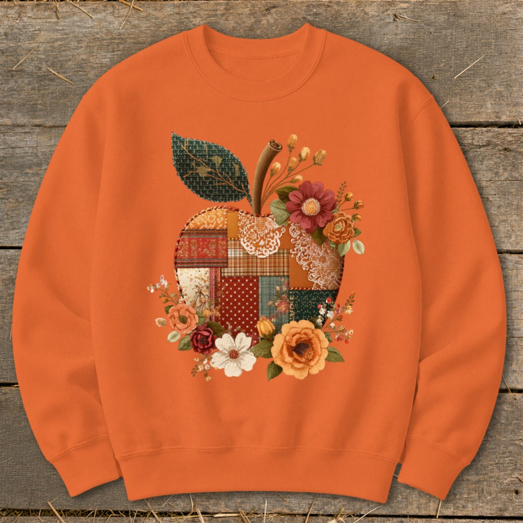 Orange sweatshirt with a patchwork apple graphic adorned with flowers and a leaf.