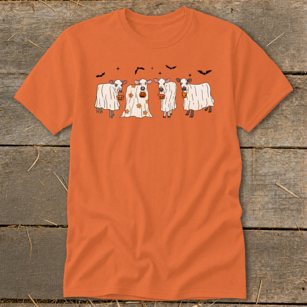 Four cows dressed as ghosts hold pumpkins under a sky with bats.