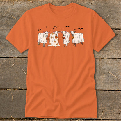 Four cows dressed as ghosts hold pumpkins under a sky with bats.