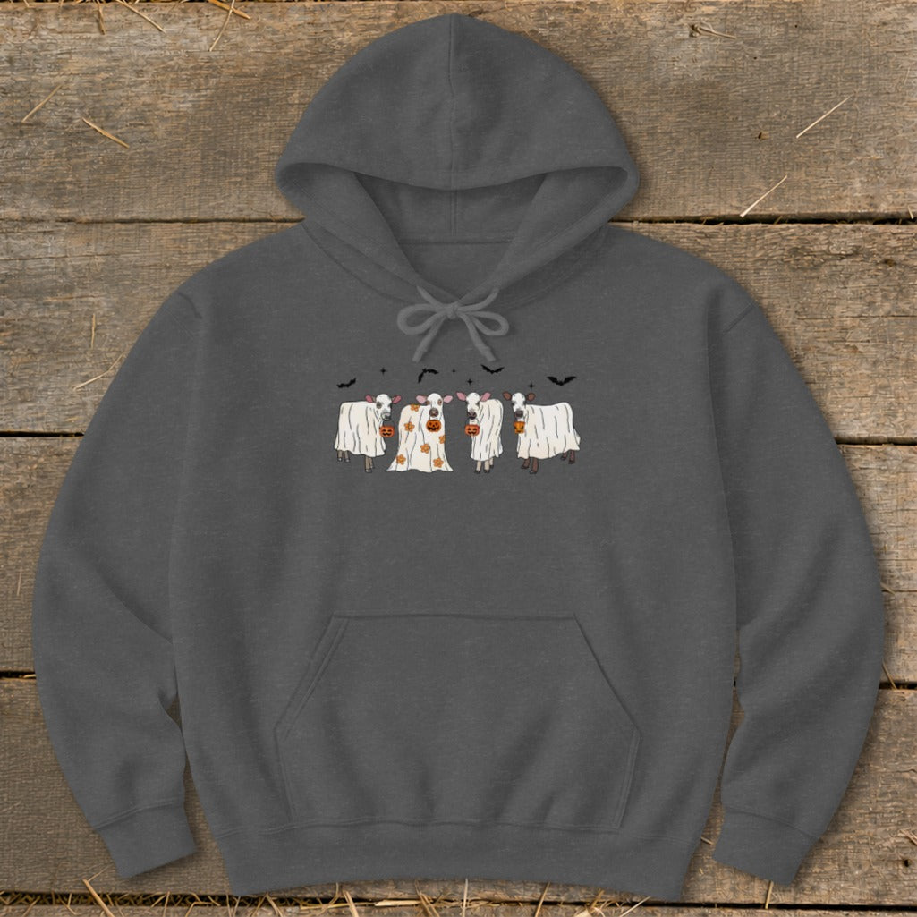 Four cows dressed as ghosts with pumpkins stand on a background of wooden planks.