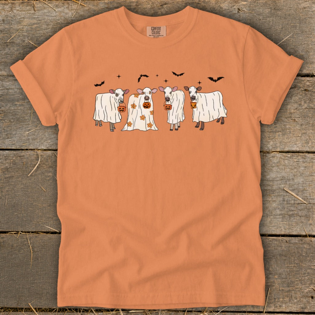 Four cows in ghost costumes carrying pumpkins with bats in the background.