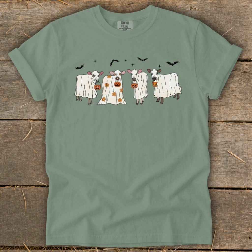 Four cows dressed as ghosts hold pumpkins, with bats in the sky.