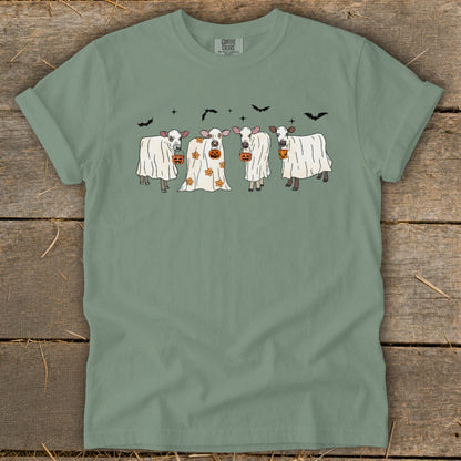 Four cows dressed as ghosts hold pumpkins, with bats in the sky.