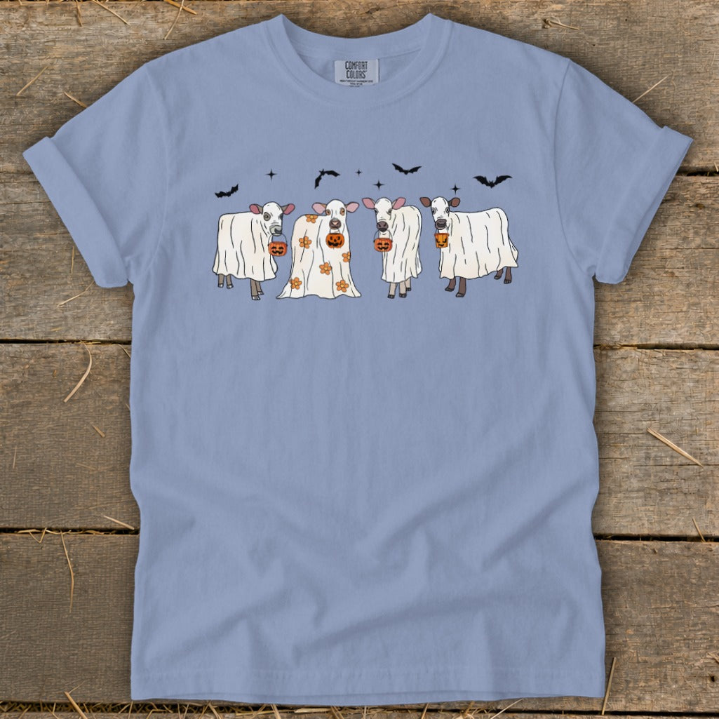 Ghost-costumed cows holding pumpkins with bats flying above.