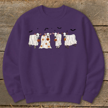 Four cows dressed as ghosts hold pumpkins against a dark background with bats.