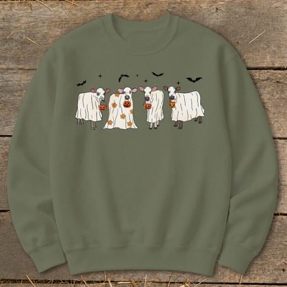 Cute cows dressed as ghosts holding pumpkins with bats above.