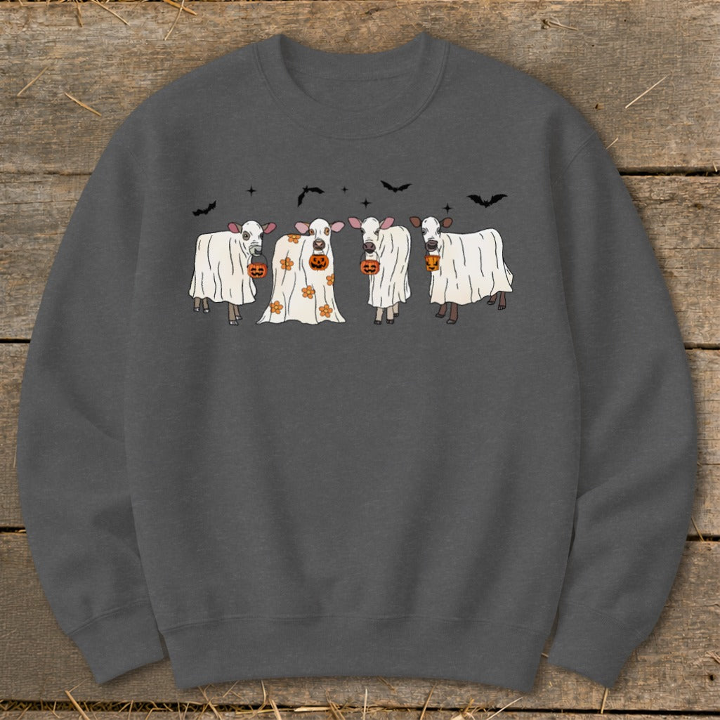 Four cows in ghost costumes holding pumpkins with bats above.