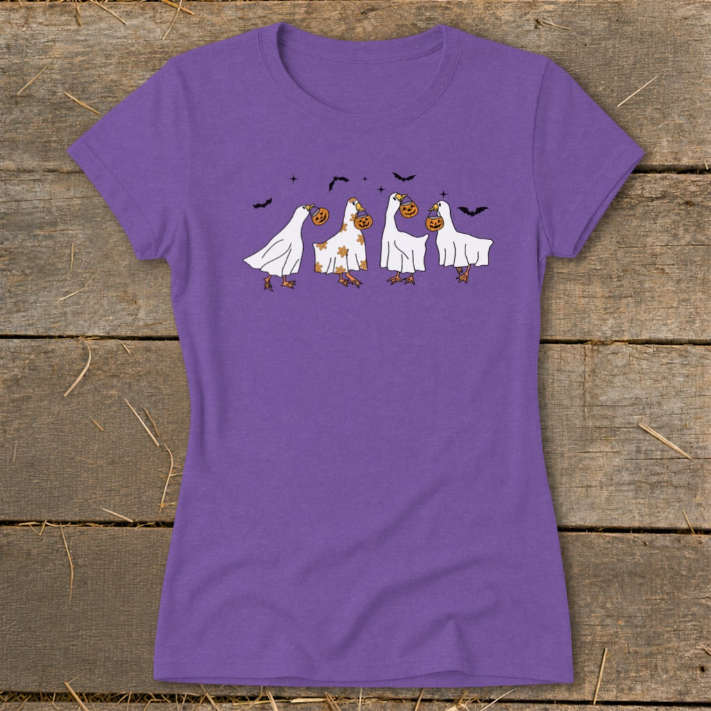 Four geese in ghost costumes with pumpkins, on a purple t-shirt.