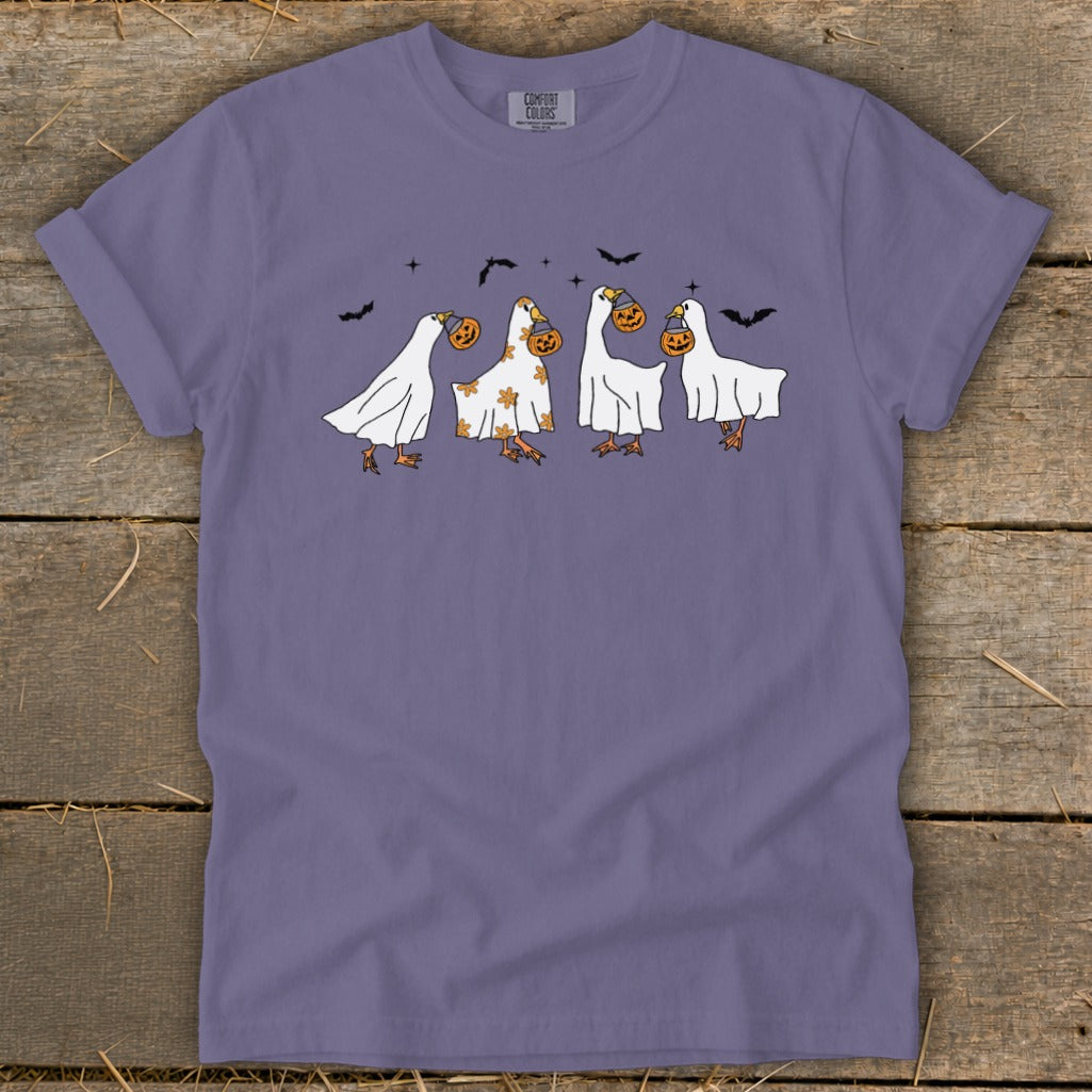 Four geese in ghost costumes carrying pumpkins on a purple t-shirt.