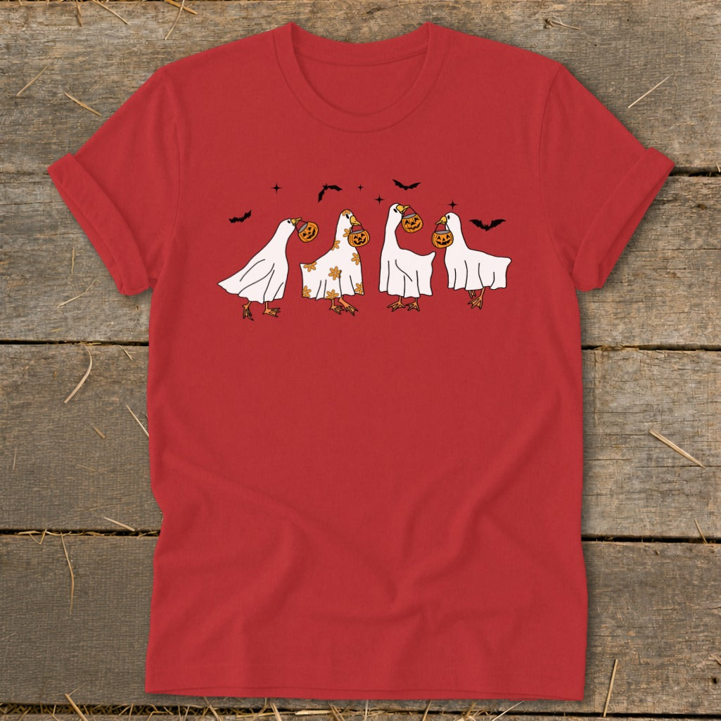 Four geese in ghost costumes carrying pumpkins and bats fly across a red shirt.