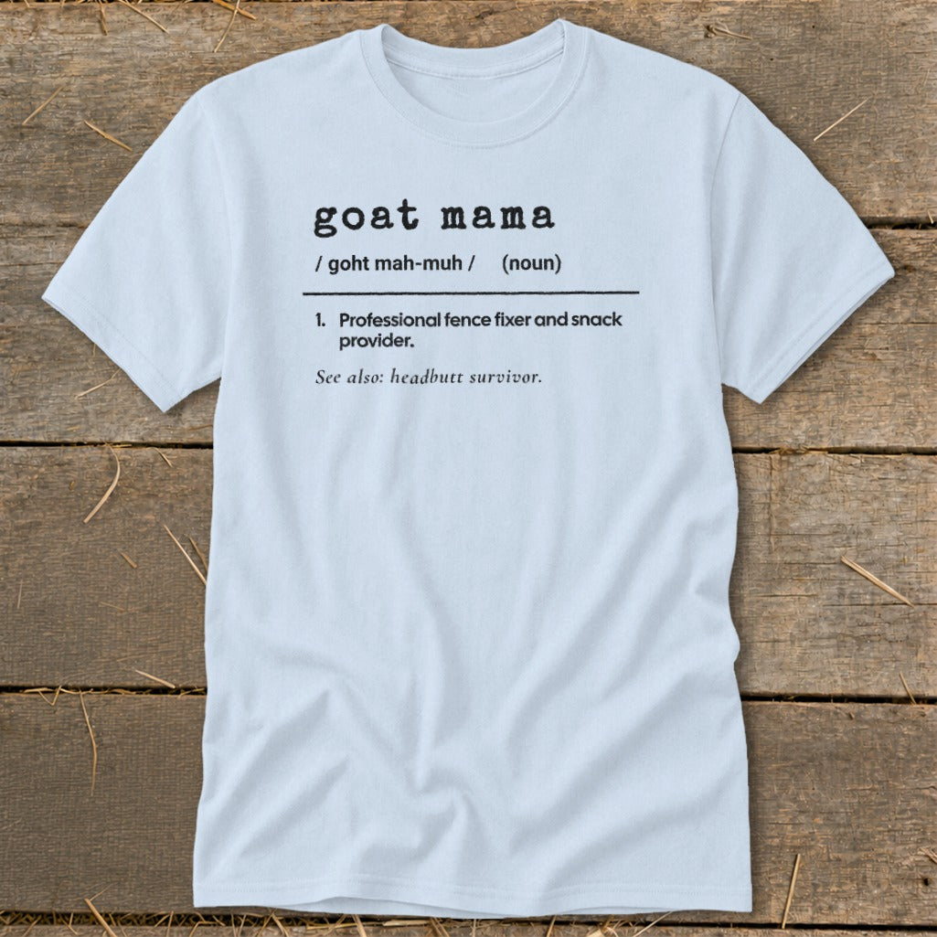 A light blue t-shirt printed with a dictionary definition for "goat mama" laid on rustic wood.
