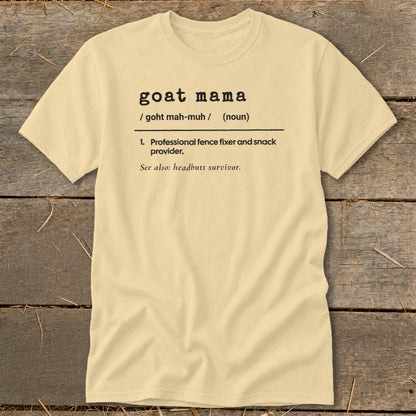 A cream-colored t-shirt on a wooden background, featuring dictionary-style text defining goat mama.