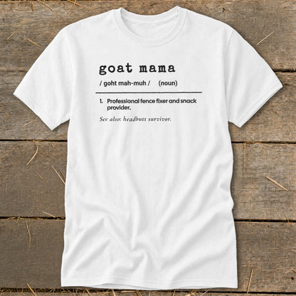 White t-shirt printed with a humorous dictionary-style definition of goat mama on a wooden background.