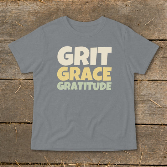 A gray short-sleeve t-shirt features the words "GRIT," "GRACE," and "GRATITUDE" printed in stacked, block lettering.
