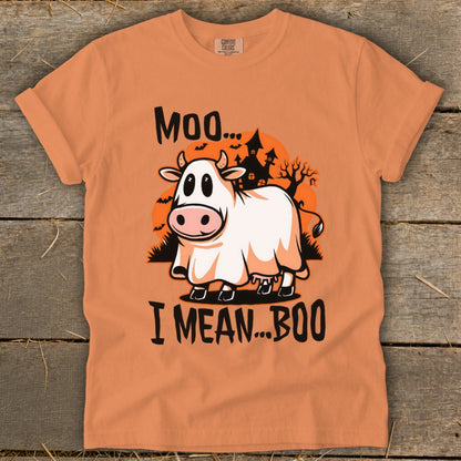 An orange t-shirt featuring a graphic of a cow in a ghost costume with the text Moo I Mean Boo.