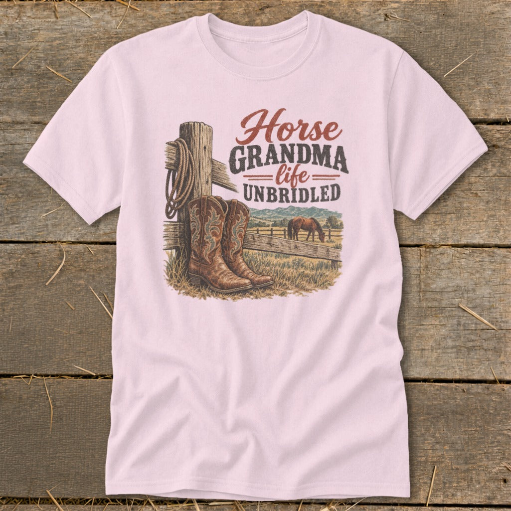 A light pink t-shirt with a graphic showing cowboy boots, a wooden fence, and the text Horse Grandma Life UNBRIDLED.