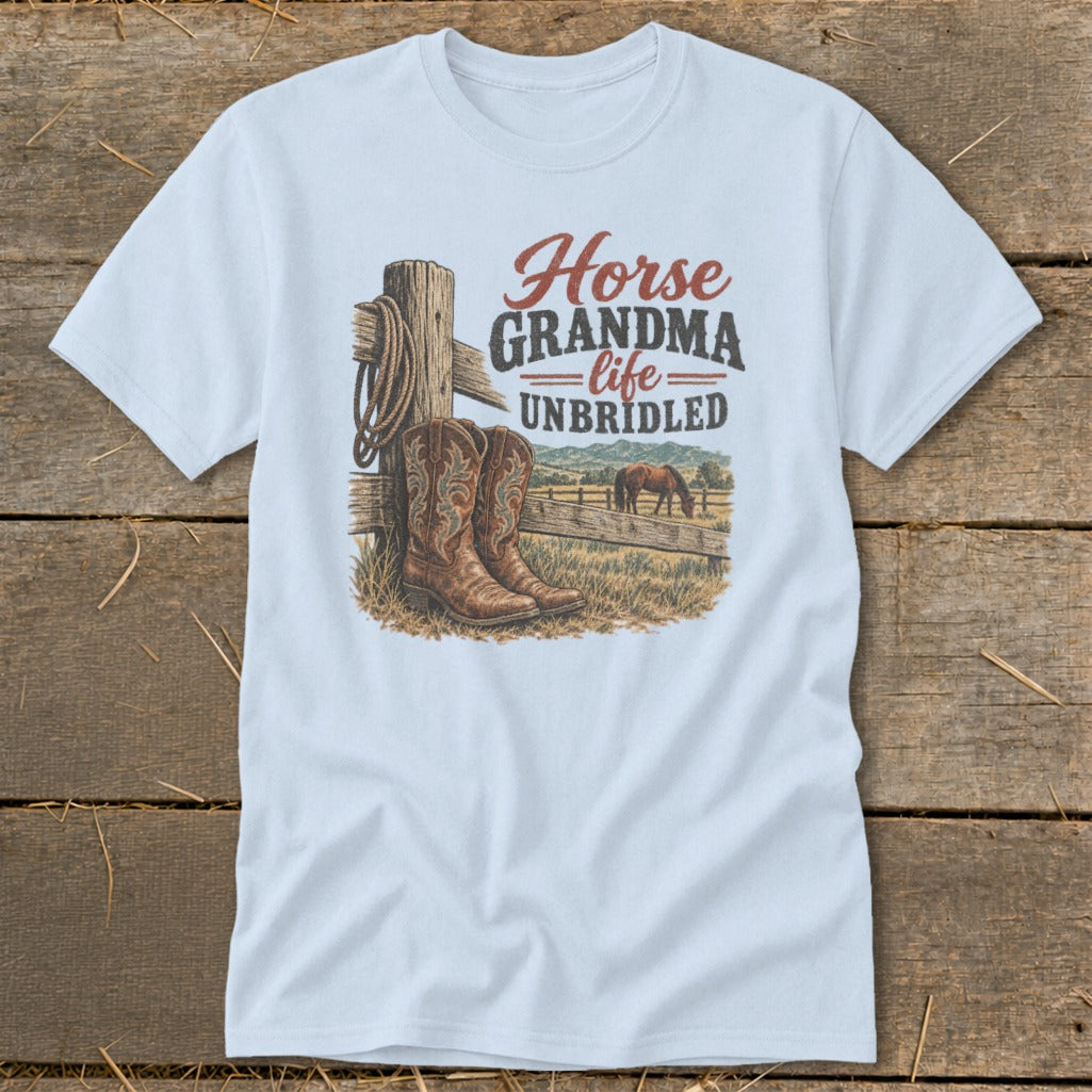 A light blue t-shirt with a graphic of cowboy boots, a horse, and the text "Horse GRANDMA life UNBRIDLED" displayed on a wooden background.