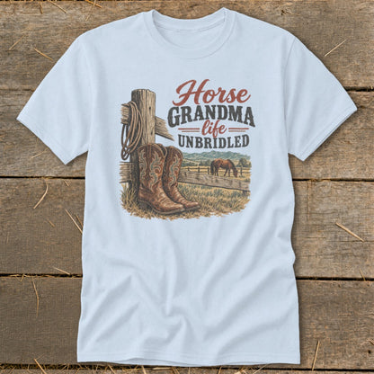 A light blue t-shirt with a graphic of cowboy boots, a horse, and the text "Horse GRANDMA life UNBRIDLED" displayed on a wooden background.