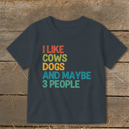 Dark grey t-shirt with text "I LIKE COWS DOGS AND MAYBE 3 PEOPLE" in retro colors.