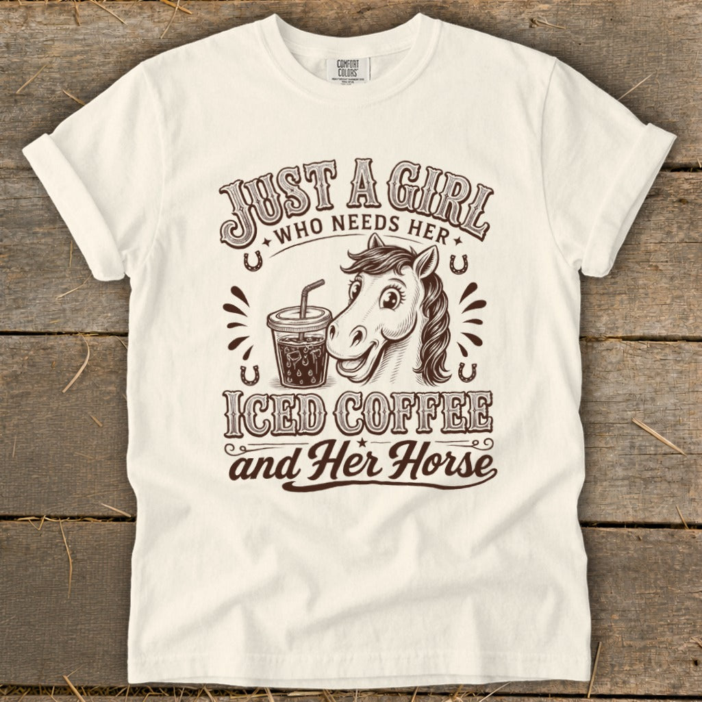 Off-white t-shirt featuring brown text reading "Just a girl who needs her iced coffee and her horse" alongside a horse and an iced coffee.