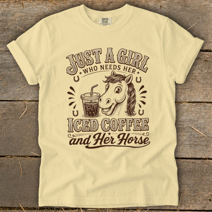 Light yellow t-shirt with a brown graphic of a horse, iced coffee, and text saying Just a girl who needs her iced coffee and her horse.